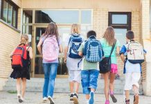 Group of children walking towards a school entrance with backpacks
