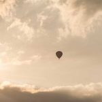 BALLOON Snags Tower—Passengers Hang 1,000 Feet A hot air balloon floating in a cloudy sky during sunset