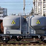A railway tank car with a nuclear warning symbol parked on tracks near urban buildings