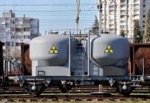 A railway tank car with a nuclear warning symbol parked on tracks near urban buildings