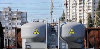 A railway tank car with a nuclear warning symbol parked on tracks near urban buildings