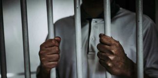 Political Star Found Dead — Husband Arrested! Person holding jail cell bars tightly.