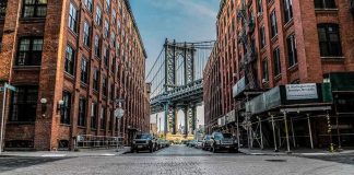 Street view with bridge between two brick buildings.