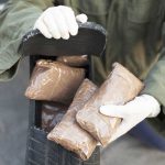 369 MILLION Lethal Doses SEIZED—Cartels Panic Person handling packages wearing gloves and green jacket.