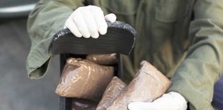 369 MILLION Lethal Doses SEIZED—Cartels Panic Person handling packages wearing gloves and green jacket.