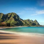 Beach with mountains and clear blue water.