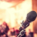 Close-up of microphone with blurred audience background.