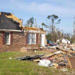 A severely damaged house with debris scattered around from a storm