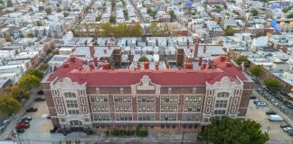 Aerial view of a large historic school building with red roof in a dense city neighborhood