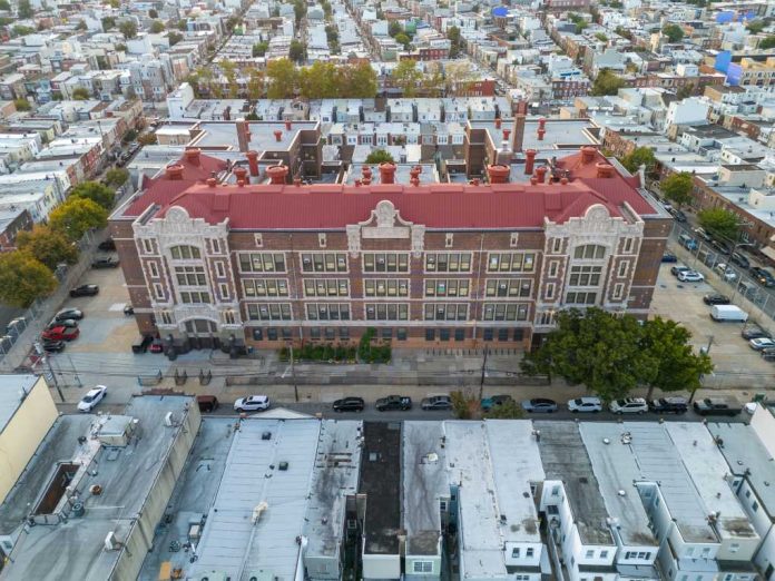 Aerial view of a large historic school building with red roof in a dense city neighborhood