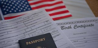 A passport and birth certificate on a table with an American flag in the background
