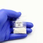 Hand in glove holding fentanyl packet with skull warning.