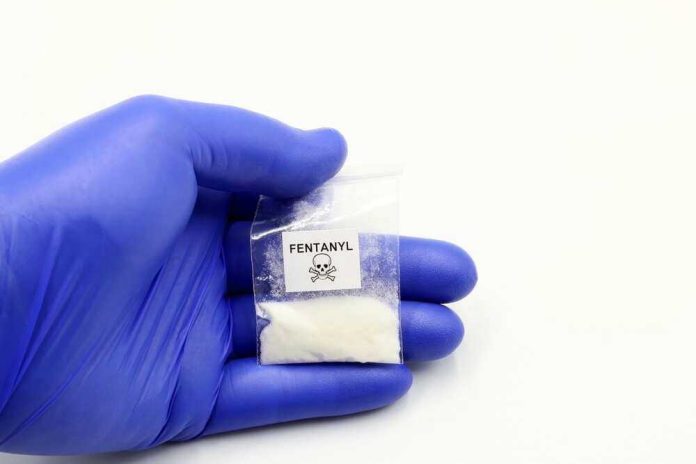 shutterstock_2334439849 Hand in glove holding fentanyl packet with skull warning.