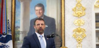 Man in suit speaking at a podium in an ornate room
