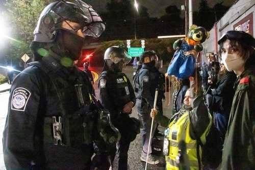 shutterstock_2688783443 Law enforcement officers facing protesters at night