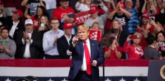 man in suit points from a stage at a political rally