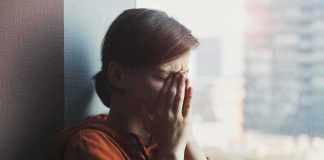 person in orange hoodie covering face by window