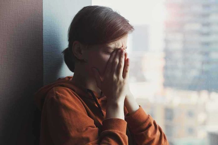 shutterstock_1733921396 person in orange hoodie covering face by window