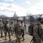 Soldiers in riot gear patrol near a fenced government building
