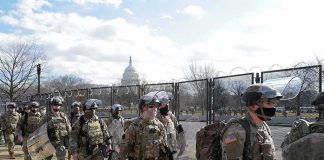 Soldiers in riot gear patrol near a fenced government building