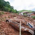 Landslide debris covering houses and a buried car on a muddy hillside