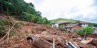 Landslide debris covering houses and a buried car on a muddy hillside