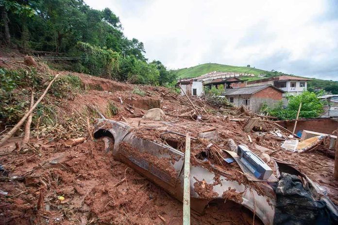Landslide debris covering houses and a buried car on a muddy hillside