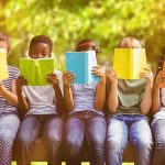 Children sitting on a bench reading colorful books outdoors