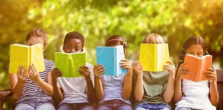 Children sitting on a bench reading colorful books outdoors