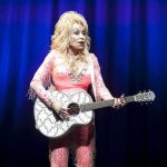 Singer in pink outfit playing a glittery acoustic guitar on stage