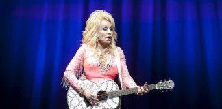 Singer in pink outfit playing a glittery acoustic guitar on stage