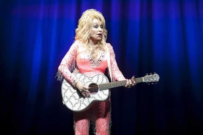 Singer in pink outfit playing a glittery acoustic guitar on stage