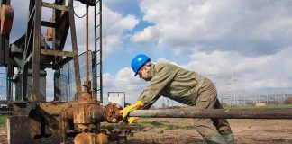 Worker in blue hard hat operating rusty oil pump equipment outdoors