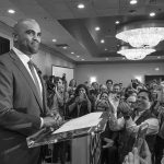 Colin Allred speaks at a podium as Christian Jones and a crowd applaud