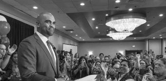 Colin Allred speaks at a podium as Christian Jones and a crowd applaud