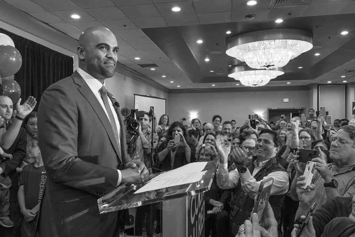Colin Allred speaks at a podium as Christian Jones and a crowd applaud