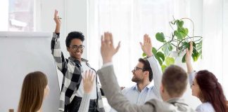 Team in meeting raising hands around smiling presenter
