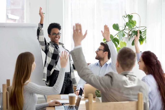 Team in meeting raising hands around smiling presenter