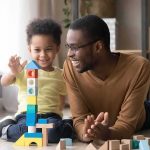 Hung Jury, Bigger Bombshell Father and child building a tall tower with colorful wooden blocks on the floor