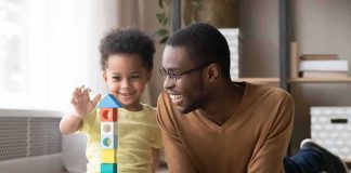 Father and child building a tall tower with colorful wooden blocks on the floor