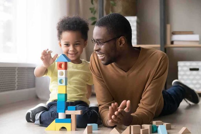 Father and child building a tall tower with colorful wooden blocks on the floor