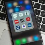 Trans Dad Essay On Father’s Day Triggers Outrage Machine Smartphone displaying a folder of news apps on a laptop keyboard