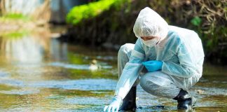 Scientist in protective suit collecting water sample from stream