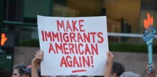 Teddy Williams at a protest holding a sign reading 'Make Immigrants American Again'