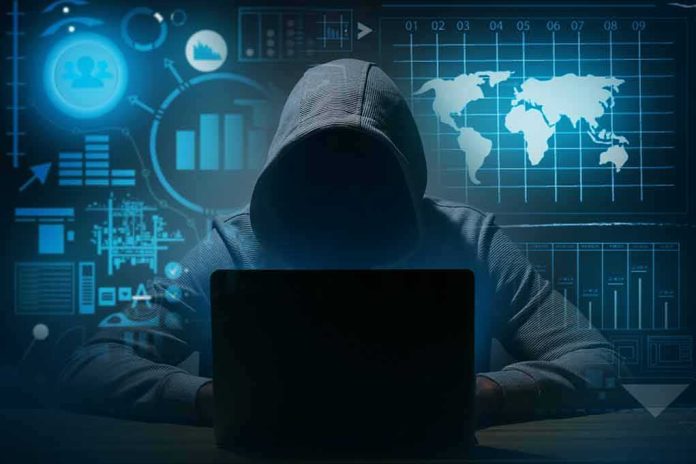 Hooded figure using a laptop in a dark room with data graphics