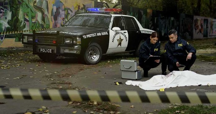 Crime scene with police car and two investigators by a covered body