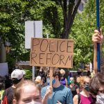 Protesters holding a cardboard sign reading Police Reform