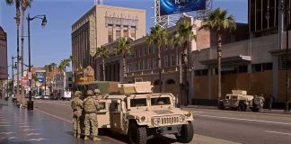 Soldiers beside a military Humvee on a palm-lined city street