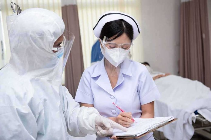 nurse in PPE writing on a clipboard with colleague