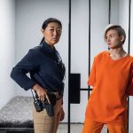 Parole Chaos: Will She Walk Monday? Police officer stands beside inmate in orange uniform inside a jail cell